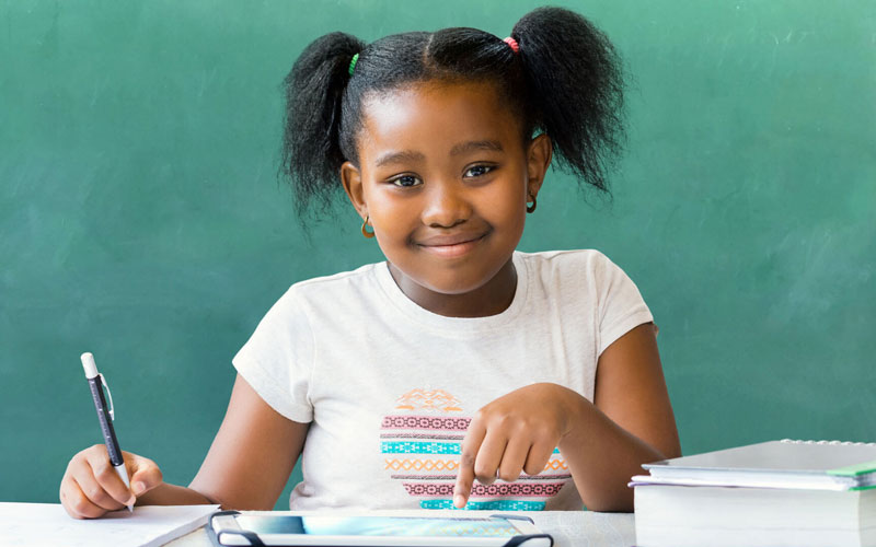 Young girl writing and pointing at tablet